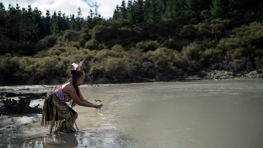 Māori woman in traditional attire collecting water from a geothermal lake at Hell’s Gate Rotorua.