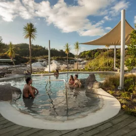Visitors soaking in a geothermal hot pool at Hell’s Gate Rotorua, shaded by canopies and native trees.