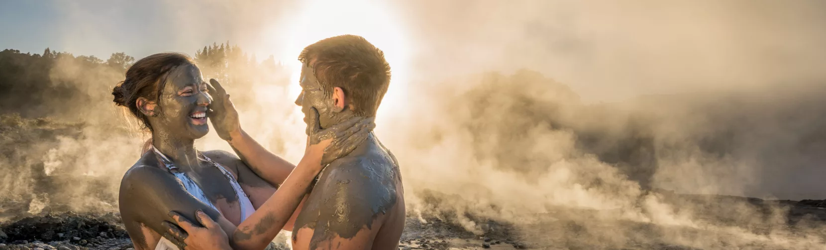 Couple enjoying a romantic mud experience at Hell’s Gate Rotorua, surrounded by steam and sunset light.