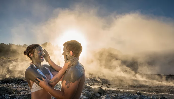 Couple enjoying a romantic mud experience at Hell’s Gate Rotorua, surrounded by steam and sunset light.