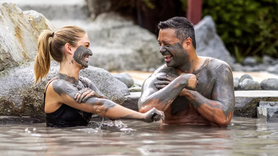 Smiling couple enjoying a mud bath together at Hell’s Gate geothermal spa in Rotorua.