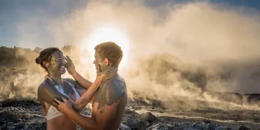 Couple enjoying a romantic mud experience at Hell’s Gate Rotorua, surrounded by steam and sunset light.
