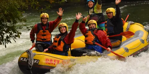 Group raising hands in excitement during rafting with Kaitiaki Adventures on the Kaituna River.