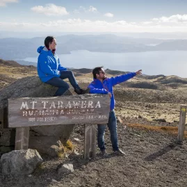 Two people beside the Mount Tarawera summit sign with sweeping views over Lake Tarawera.