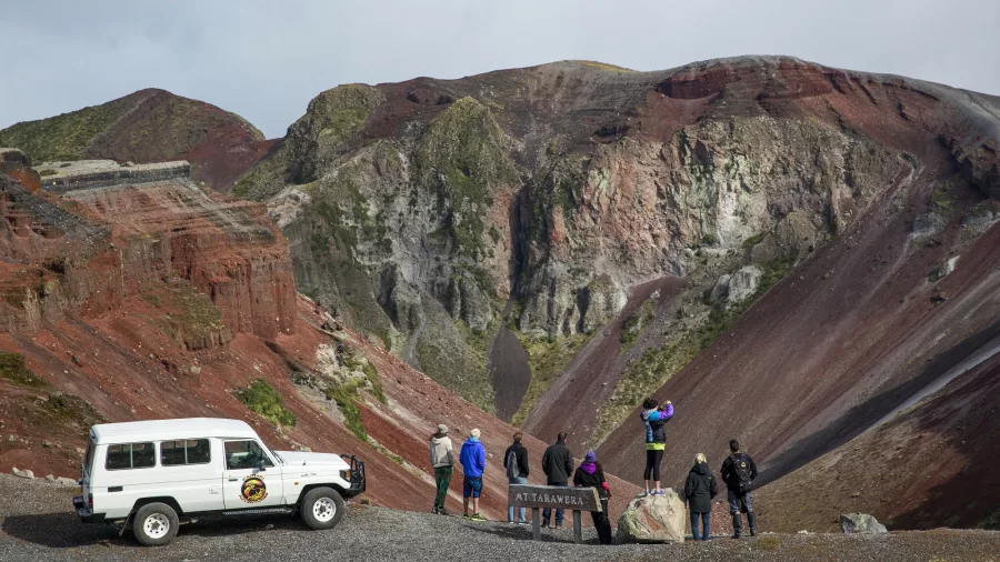 Group at a lookout point over the Mount Tarawera crater, with 4WD vehicle parked nearby.