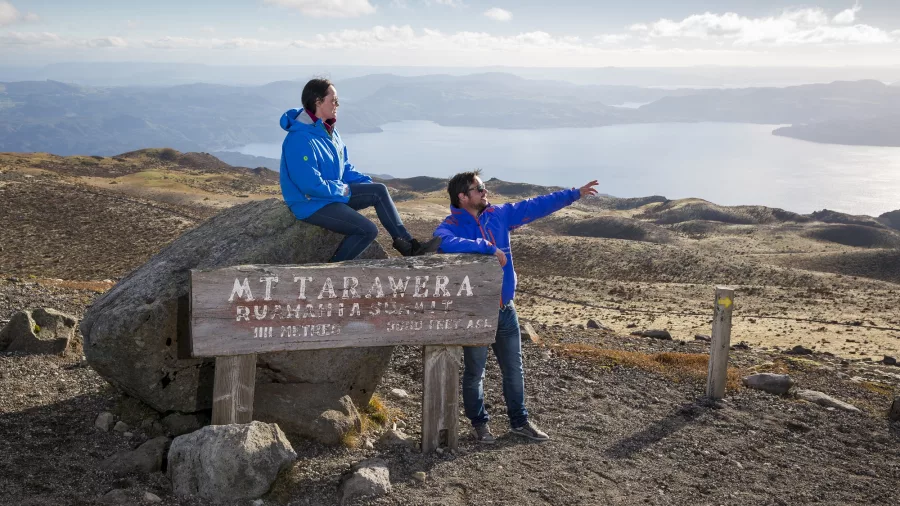 Two people beside the Mount Tarawera summit sign with sweeping views over Lake Tarawera.