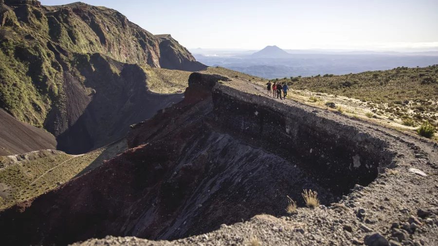 Guided hikers walking along the edge of Mount Tarawera's crater with panoramic volcanic views.