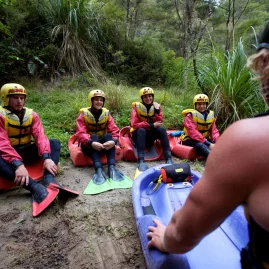 Instructor giving a safety briefing to sledging participants on the riverbank at Kaituna.