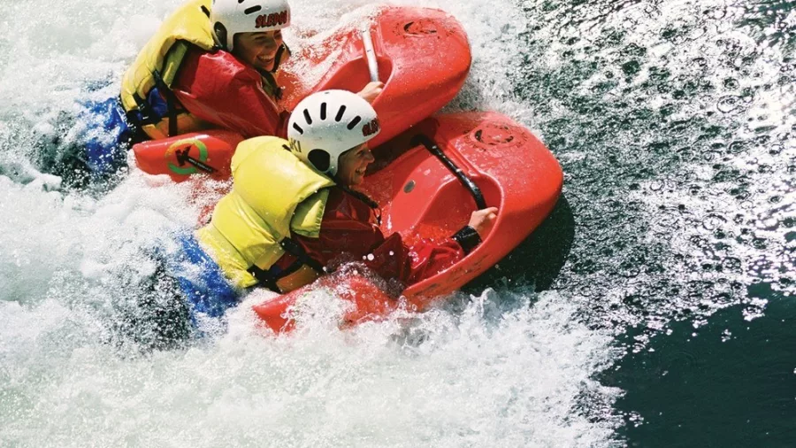 Two women sledging side-by-side down a white-water rapid on the Kaituna River.