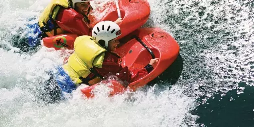 Two women sledging side-by-side down a white-water rapid on the Kaituna River.