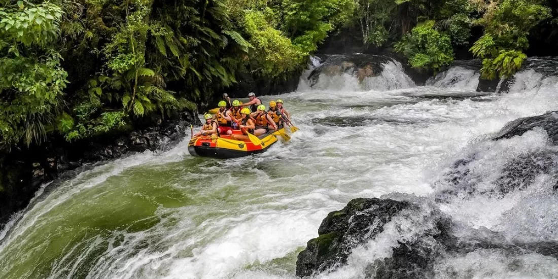 Rafters preparing to descend Tutea Falls on the Kaituna River, surrounded by lush native forest in Rotorua.