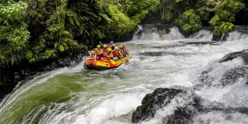 Rafters preparing to descend Tutea Falls on the Kaituna River, surrounded by lush native forest in Rotorua.