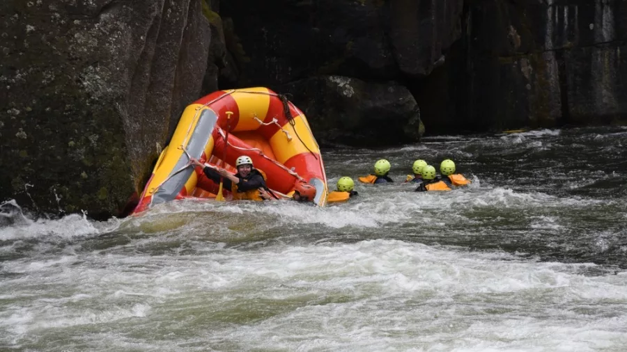 Raft flipped in rapid while crew members swim nearby on the Wairoa River.