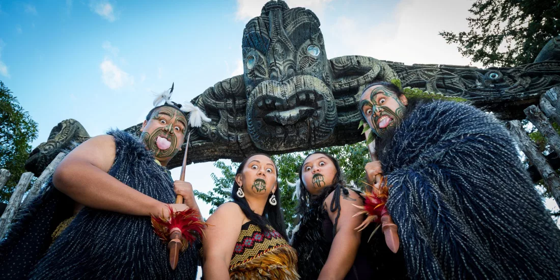 Group of Māori performers in traditional attire standing under carved entrance at Mitai Māori Village.