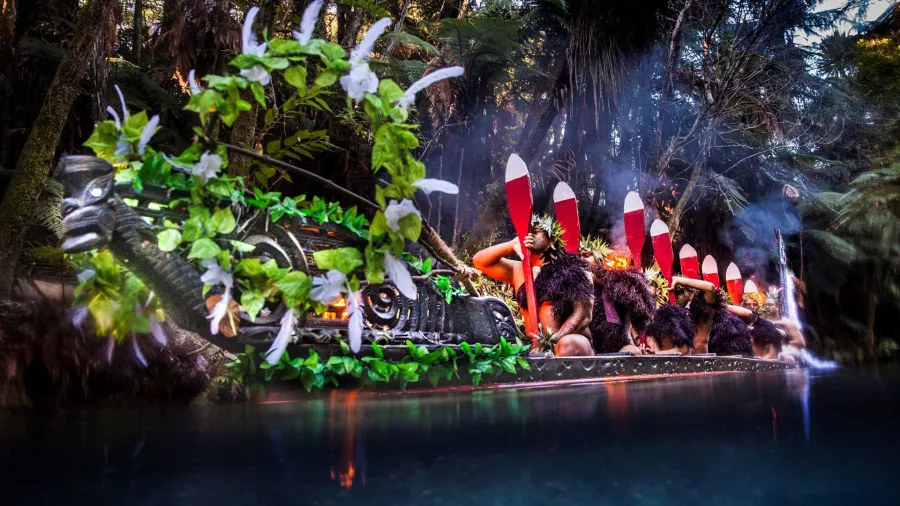 Traditional Māori waka decorated with ferns and feathers arriving at Mitai Māori Village during the cultural welcome ceremony.