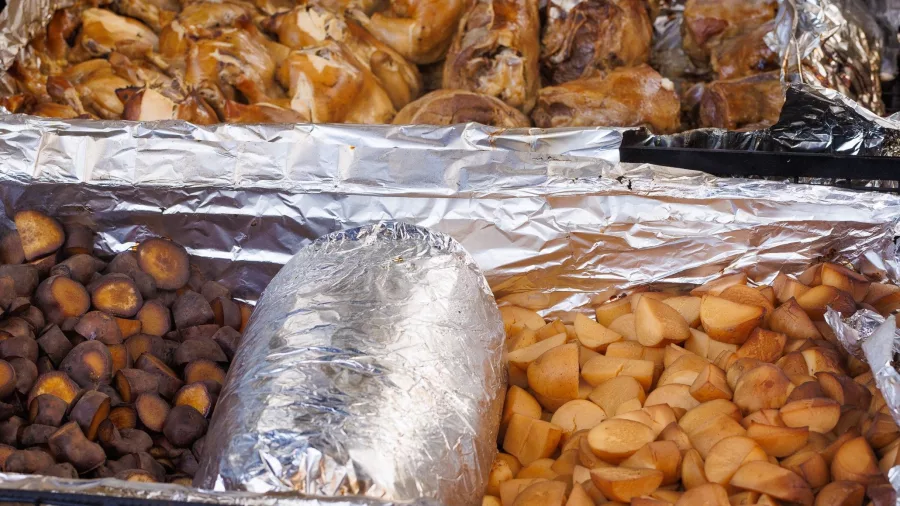 Cooked meat, kūmara and vegetables in foil trays inside a traditional hangi pit at Mitai Māori Village.