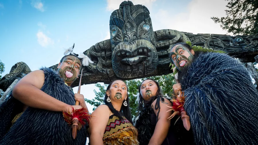 Group of Māori performers in traditional attire standing under carved entrance at Mitai Māori Village.