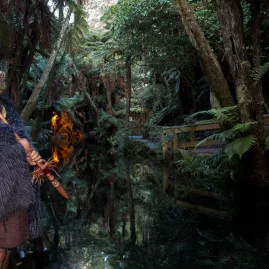 Māori warrior standing beside a stream during a twilight tour at Mitai Māori Village.