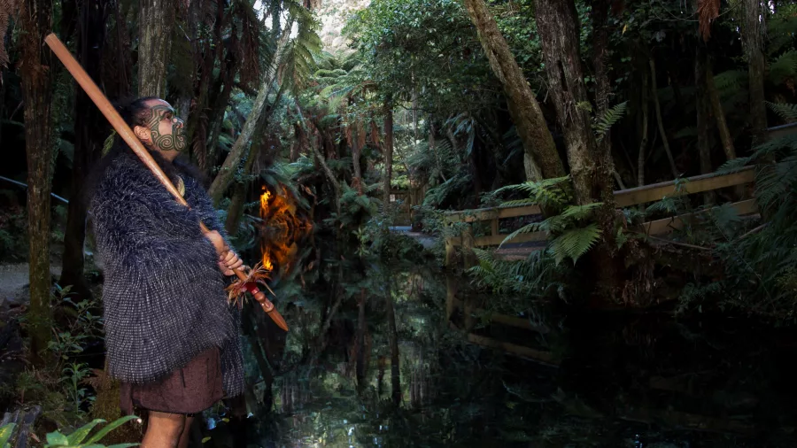 Māori warrior standing beside a stream during a twilight tour at Mitai Māori Village.