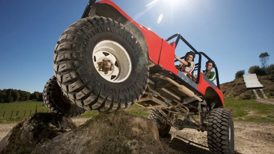 Off Road NZ’s red 4X4 climbing a large rock mound under the Rotorua sun.