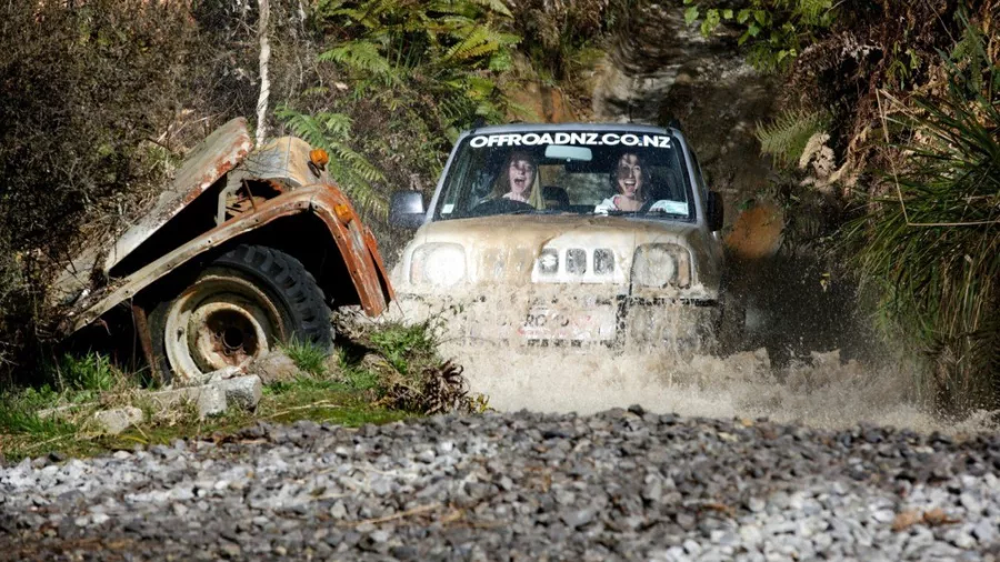 4WD vehicle splashing through muddy terrain at Off Road NZ, passing a rusty obstacle.