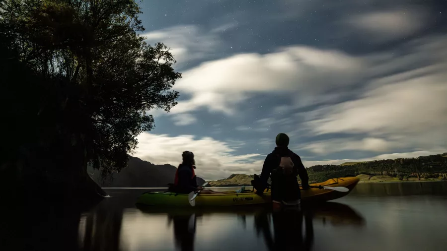 Two kayakers floating on Lake Okareka at dusk during a glow worm tour in Rotorua.