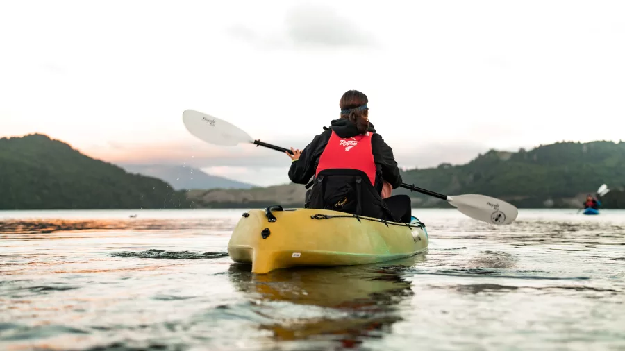 Person kayaking across Lake Okareka at sunset on a glow worm tour in Rotorua.