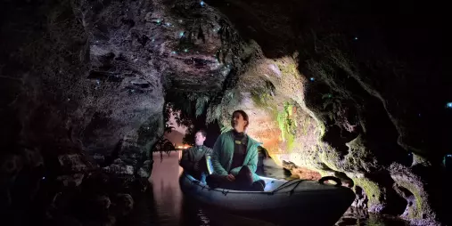Couple in a kayak exploring an illuminated glow worm cave in Rotorua.