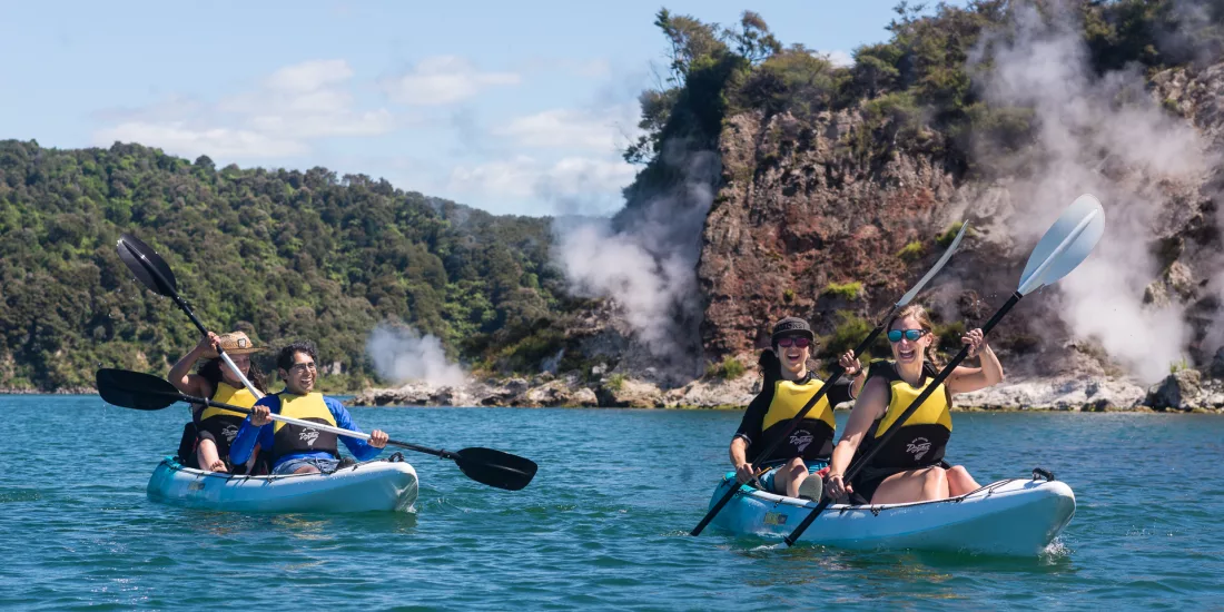 Kayakers paddling past geothermal steam vents along the shores of Lake Rotomahana.