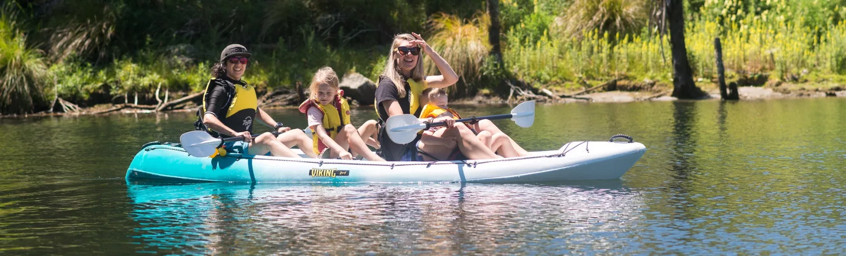 Family kayaking on calm waters surrounded by native bush in Waimangu Volcanic Valley.