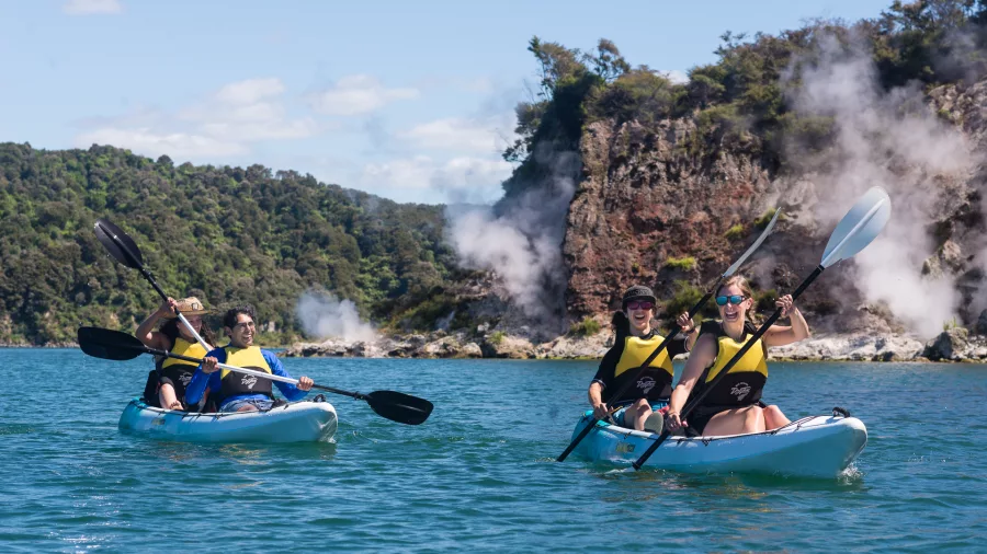Two kayaks paddling along Lake Rotomahana’s steaming volcanic cliffs in Waimangu Valley.