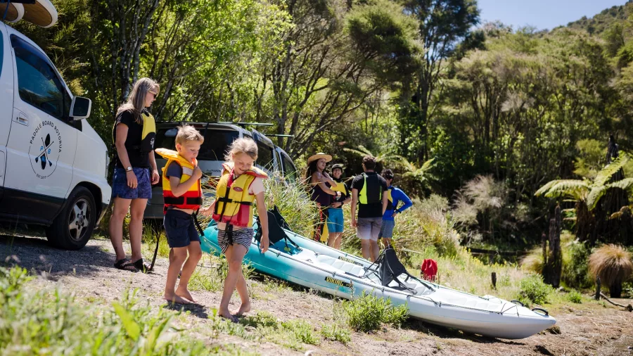 Family preparing kayaks at the launch site surrounded by native forest near Lake Rotomahana.