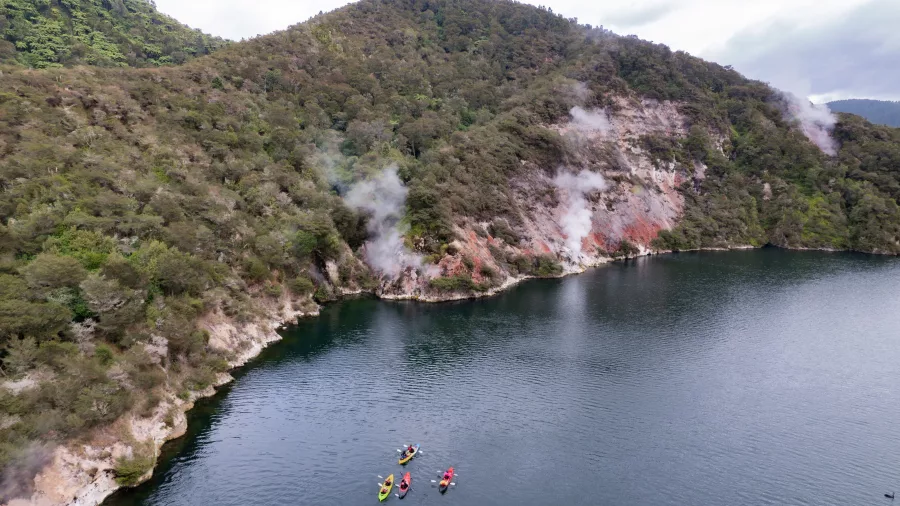Group of kayaks floating on Lake Rotomahana near geothermal shoreline vents.