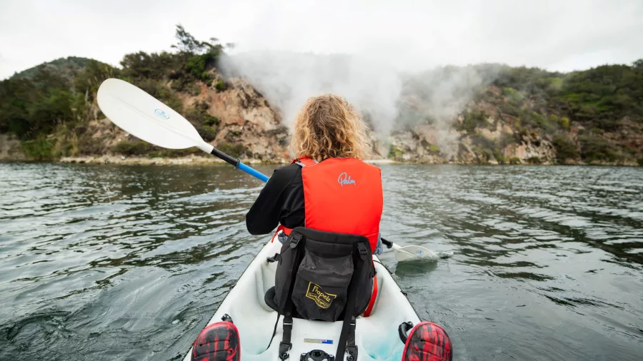 A kayaker paddling towards steaming cliffs on Lake Rotomahana, Waimangu Volcanic Valley.