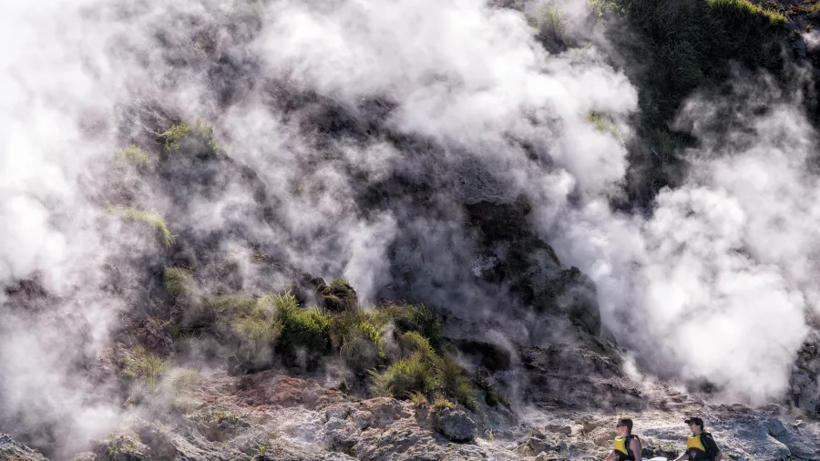 Two kayakers floating beside the geothermal cliffs of Lake Rotomahana in Rotorua.