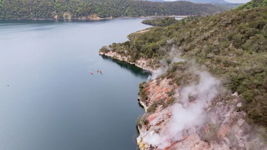 Kayakers paddling past steaming cliffs along the edge of Lake Rotomahana, Rotorua.