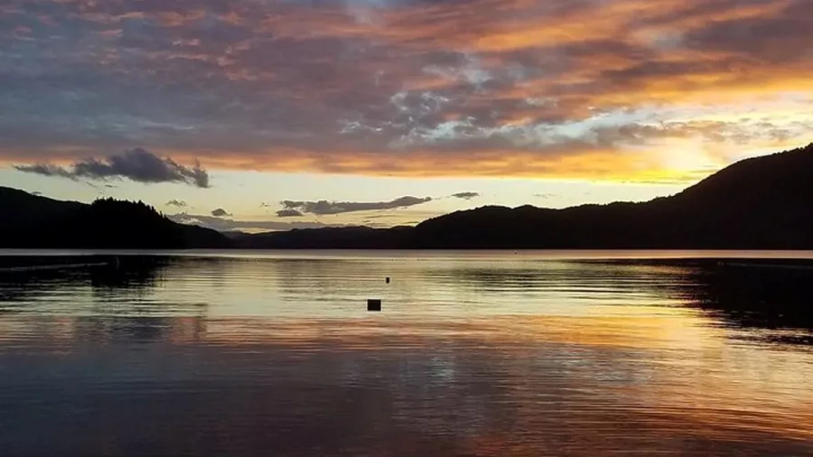 Sunset casting warm colours over the calm waters of Lake Ōkāreka in Rotorua.
