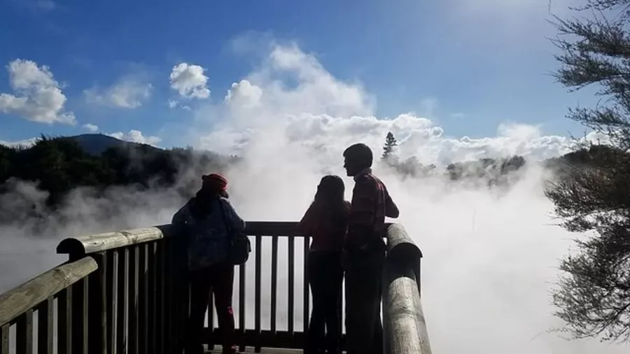 Silhouetted visitors standing in steam on a wooden platform at a Rotorua geothermal site.