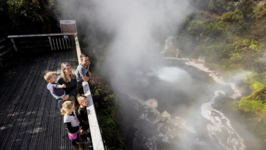 Family on a wooden lookout platform overlooking a steaming geothermal feature in Rotorua