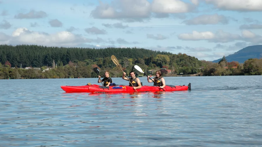 Three friends kayaking across the calm waters of Lake Rotoiti on a sunny day with River Rats.