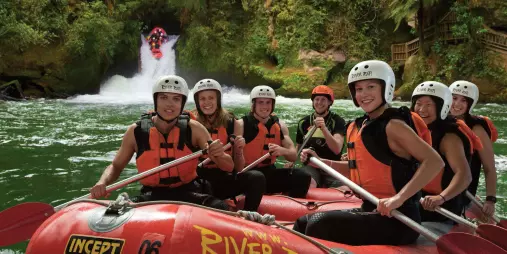 Happy rafting crew posing in front of Tutea Falls on the Kaituna River with River Rats.