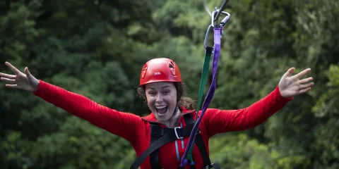 Tour guest enjoys thrilling zipline ride with arms outstretched in Rotorua’s native forest canopy adventure