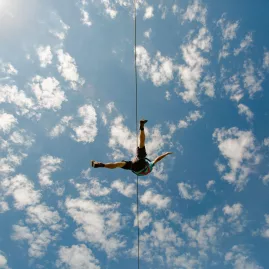 Zipliner silhouetted against a bright blue sky filled with clouds in Rotorua