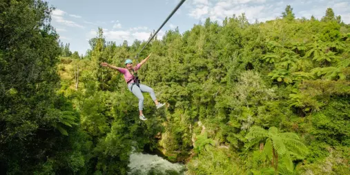 Woman ziplining high above Kaituna River gorge surrounded by lush native forest
