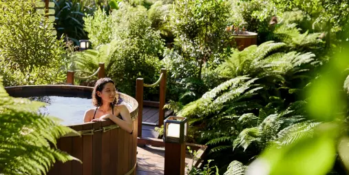 Guest relaxing in a private cedar hot tub surrounded by native ferns and gardens at Secret Spot Rotorua