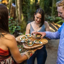 Guests sampling traditional Māori kai served outdoors by a Te Pā Tū host