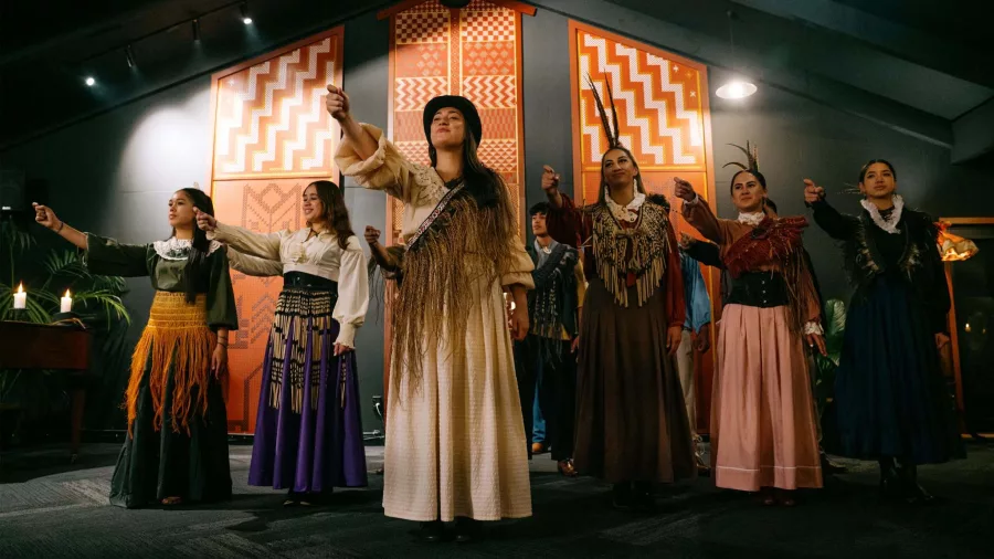 Group of Māori women in traditional and colonial-era dress performing indoors at Te Pā Tū