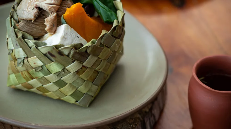 Traditional hāngī meal with meat and vegetables served in a woven flax basket at Te Pā Tū