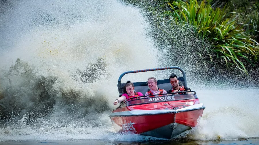 Agrojet boat racing through the water creating a huge spray, passengers cheering