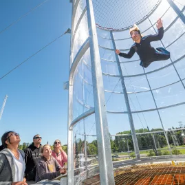 Visitor flying in a vertical wind tunnel at Freefall Xtreme while friends watch from below